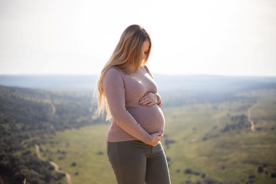 Katharina stands on a hilltop, cradling her baby bump while gazing down at the vast, sunlit wilderness during her babymoon safari.